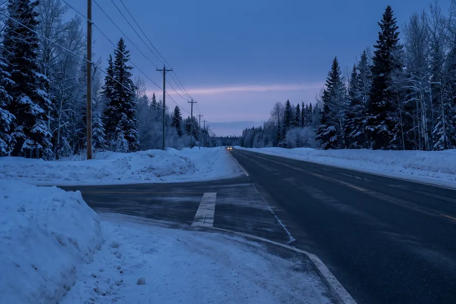 Two-lane highway through snowy forest at dusk